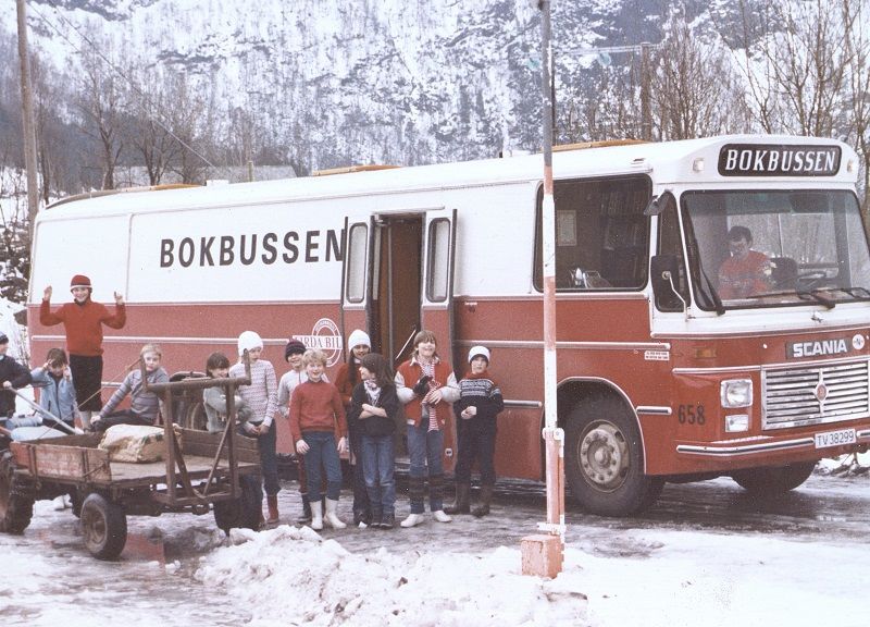 Bilete av gamal buss med ei gruppe med born framfor. Vinterlandskap.