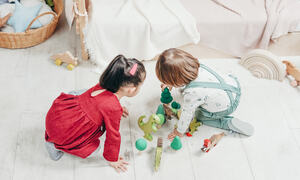 To små barn som leker med treleker på hvitt gulv.