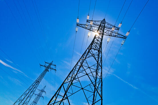 electricity pylon against blue sky with sun
