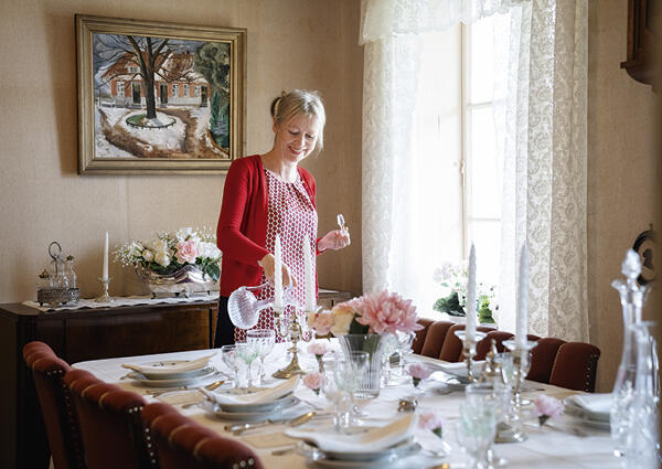 Konservator Trude Eriksen ved Museum Stavanger i spisestuen på Holmeegenes. Her er det dekket til fest og meny-kortene viser at gjestene fikk både flyndrefilet og ryper. Foto: Marie von Krogh/MUST.