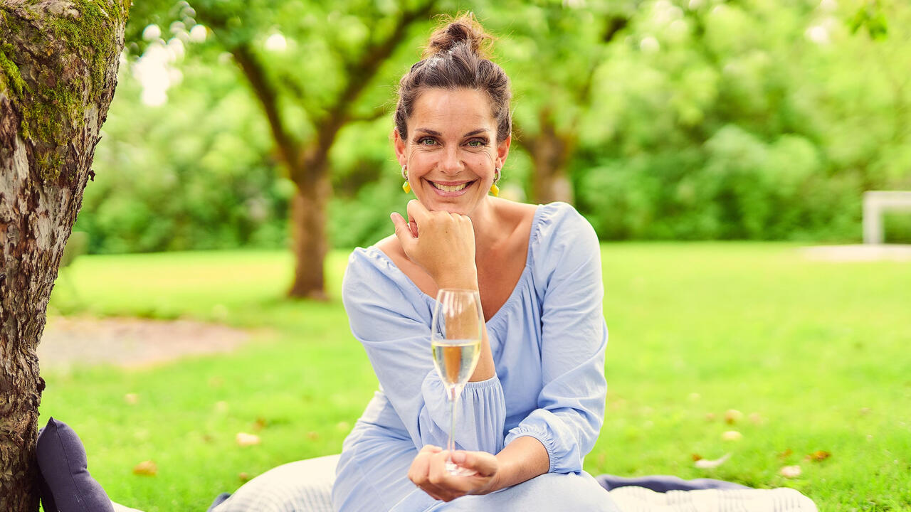 Foto av Sara Døscher som sitter i en hage med et glass vin i hånden