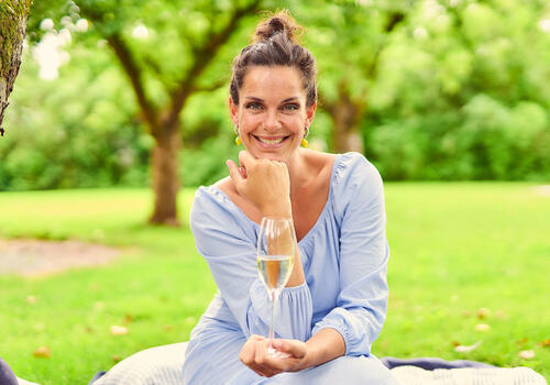 Foto av Sara Døscher som sitter i en hage med et glass vin i hånden