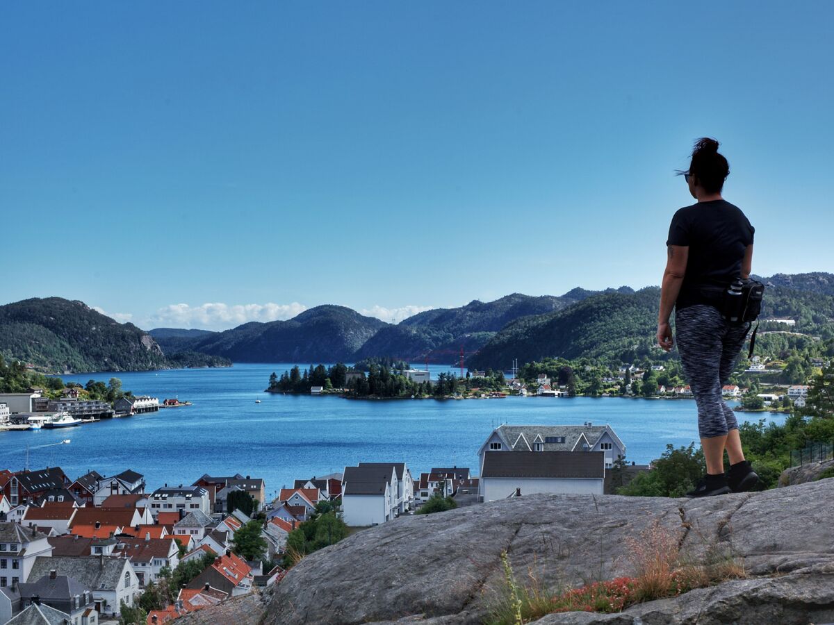 Kvinne med ryggen mot kamera som ser utover utsiktspunktet på Lilleheia, mot Flekkefjord sentrum. Blå himmel.