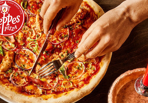 Bildet viser et par hender som skjærer opp en pizza