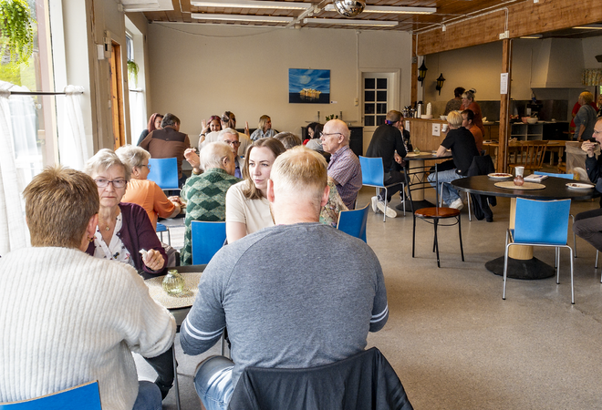 Grupper mennesker sitter ved kafebord i de gamle lokalene til Heen-butikken på Inndyr. Elever fra voksenopplæringa selger kaffe og kaker.