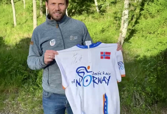 Thor Hushovd holder en Arctic Race t-skjorte. Bakgrunnen er et sommerlig skogslandskap.