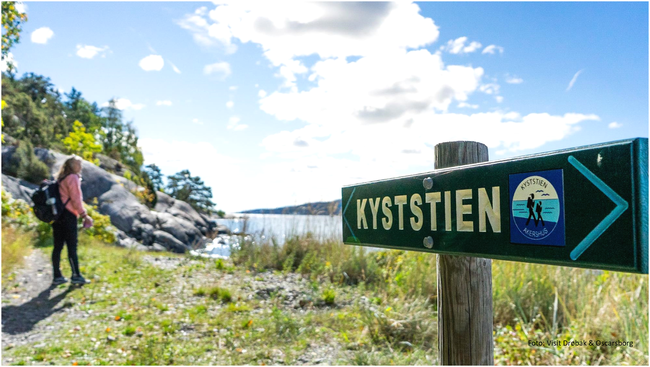 Skilt med tekst kyststien med en person i bakgrunnen, natur, sjø og blå himmel