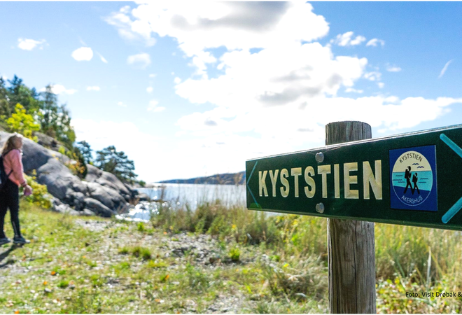 Skilt med tekst kyststien med en person i bakgrunnen, natur, sjø og blå himmel