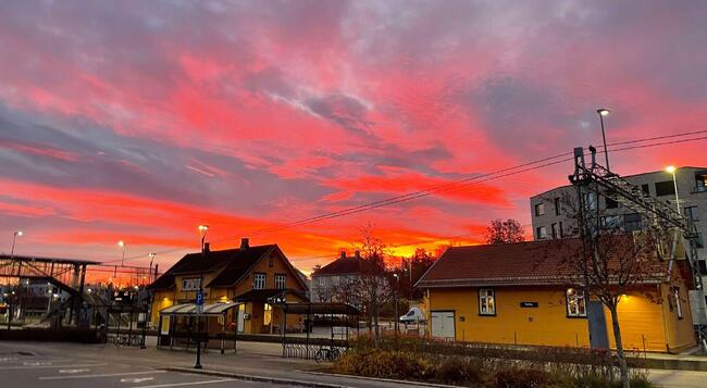 Togstasjon, to gule bygg, rød himmel