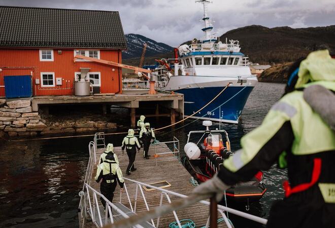 Fiskebåt oog brygge med fem gulkledde mennesker på ei flytebrygge