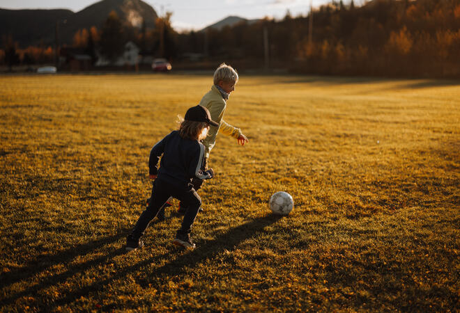 Barn som sparker ball i kveldssol