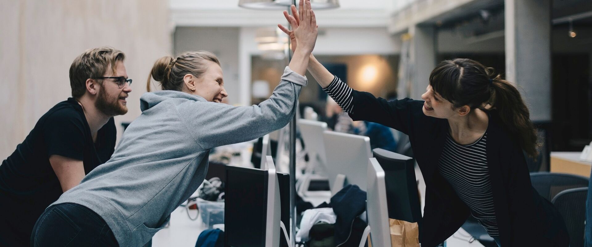 Tre personer i et kontorlandskap. To av dem gjør high five.